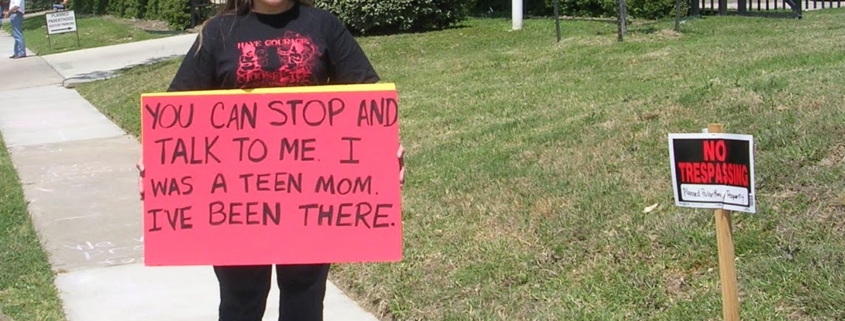 Woman holds a sign that reads "You can stop and talk to me. I was a teen mom. I've been there."
