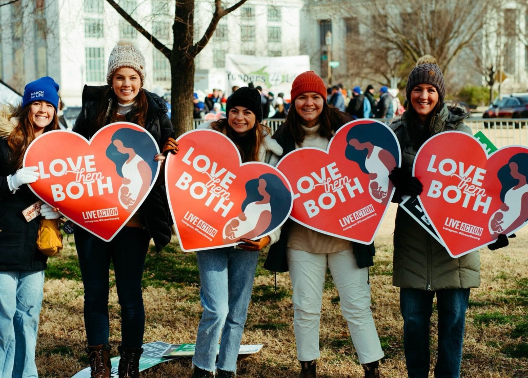 Young women holding "Love Them Both" signs
