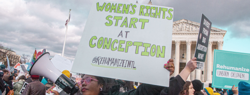 Pro-life advocate holds sign outside Supreme Court that reads "Women's rights start at conception"