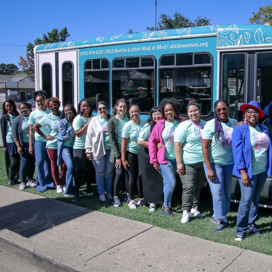 Abide Women's Health staff and volunteers stand in a line outside Abide's van